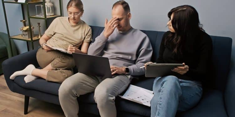 three people working on sofa looking stressed