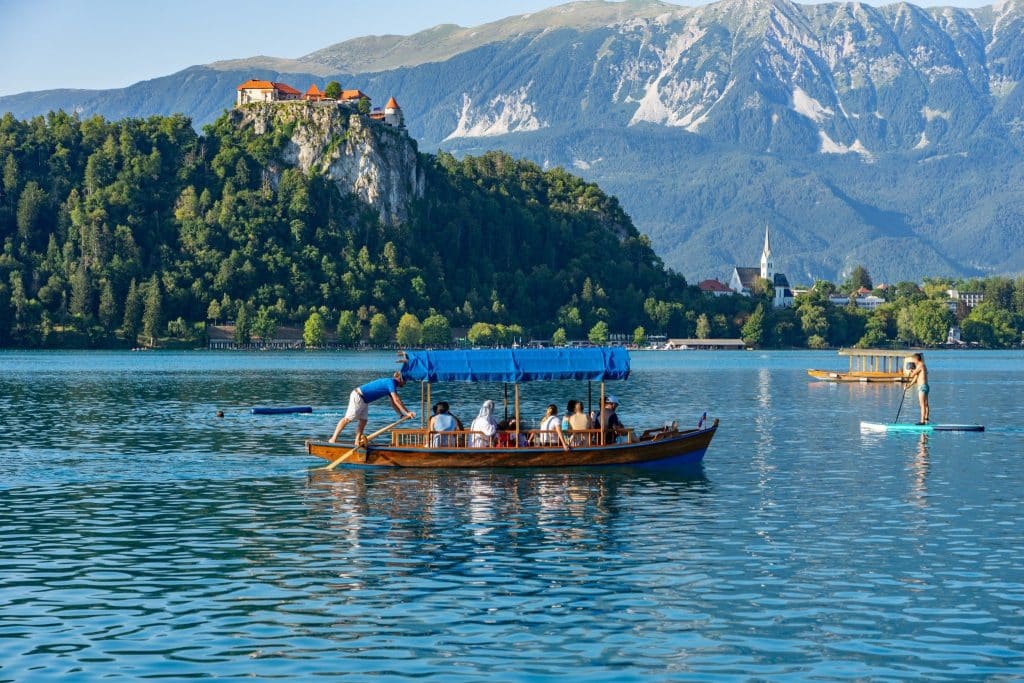 Pletna boat on Lake Bled travel with castle and mountains in view.