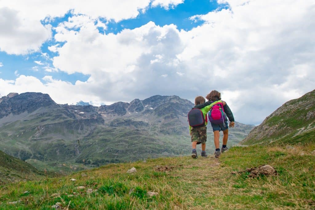 Children hiking in mountain valley with backpacks