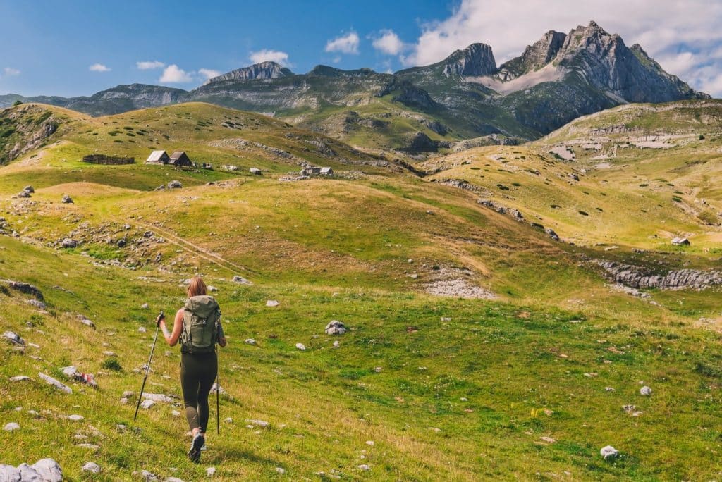 Backpacker trekking across green hills on Montenegro travel adventure