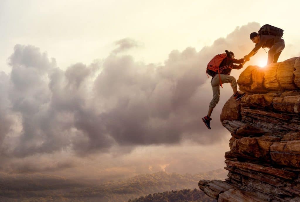 two hikers helping on rocky ledge at dusk