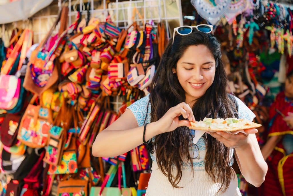 Young woman enjoying fresh street food at a colorful market, highlighting how local cuisine helps stretch a solo travel budget.