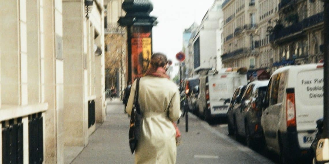 a woman walking down a street next to parked cars