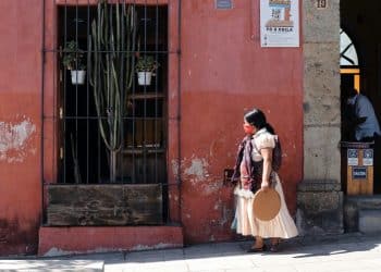 a woman walking down a street past a red building